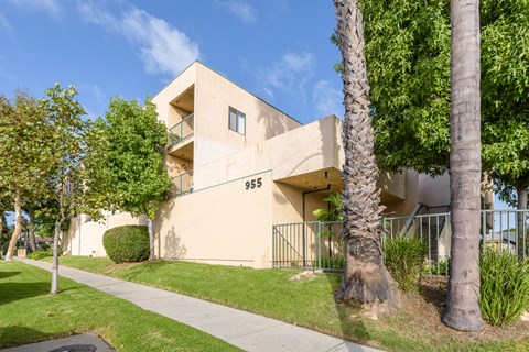 a beige apartment building with trees and a sidewalk