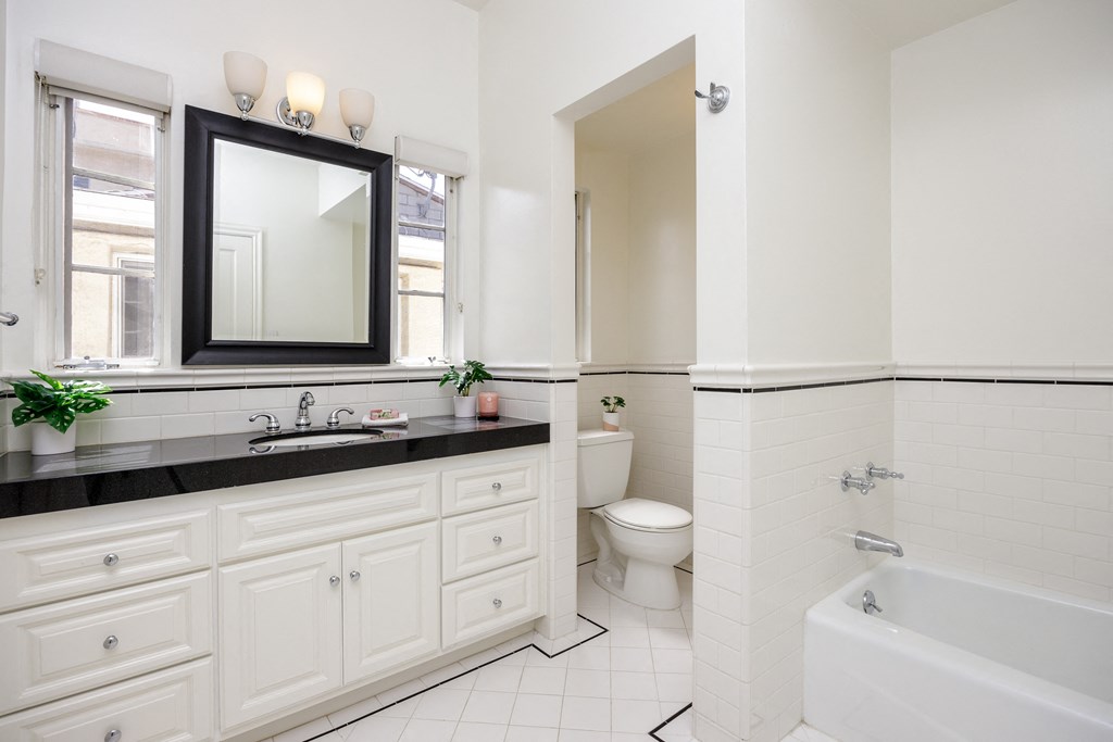 a bathroom with white cabinets and a black counter top and a tub and a toilet