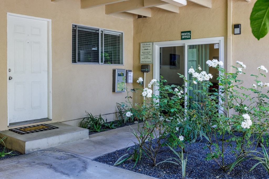 the front door of a beige building with white flowers