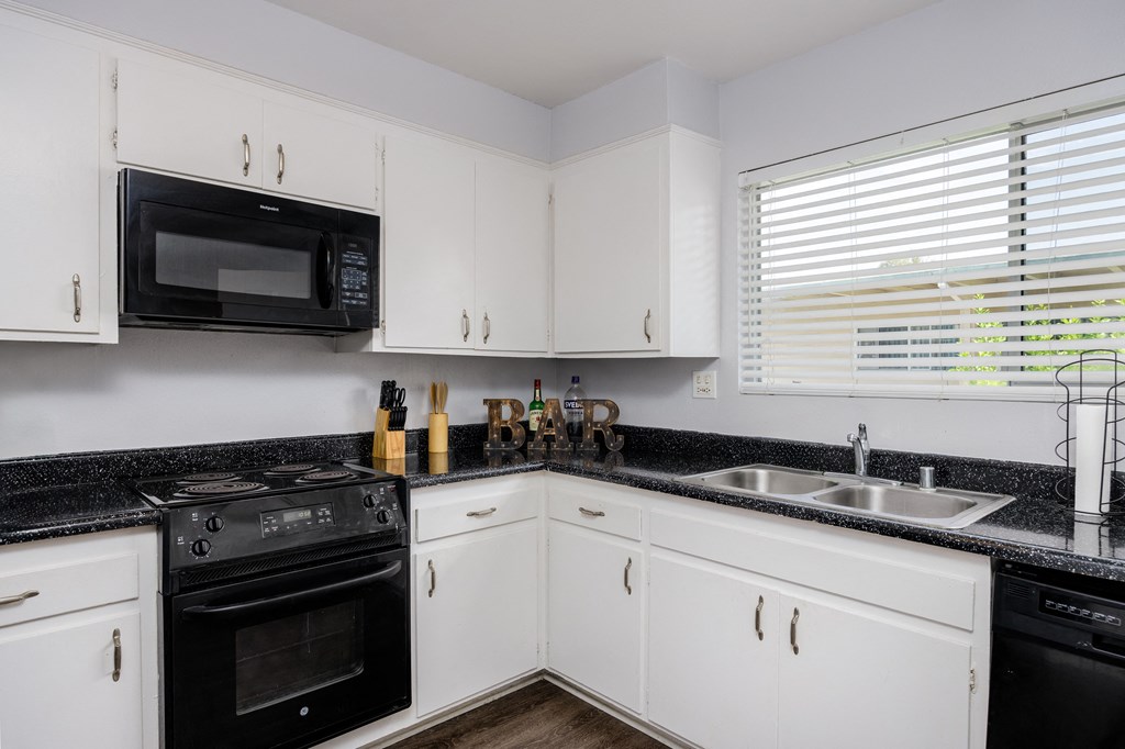 a kitchen with white cabinets and black counter tops and black appliances