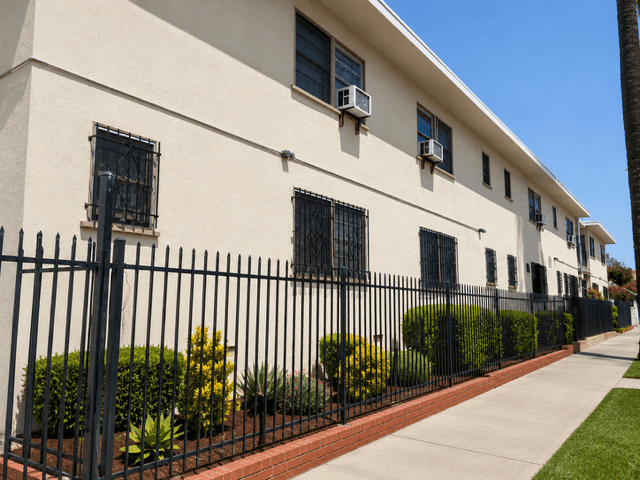 A white building with black iron fencing and bushes in front.