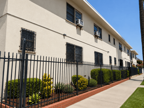 A white building with black iron fencing and bushes in front.
