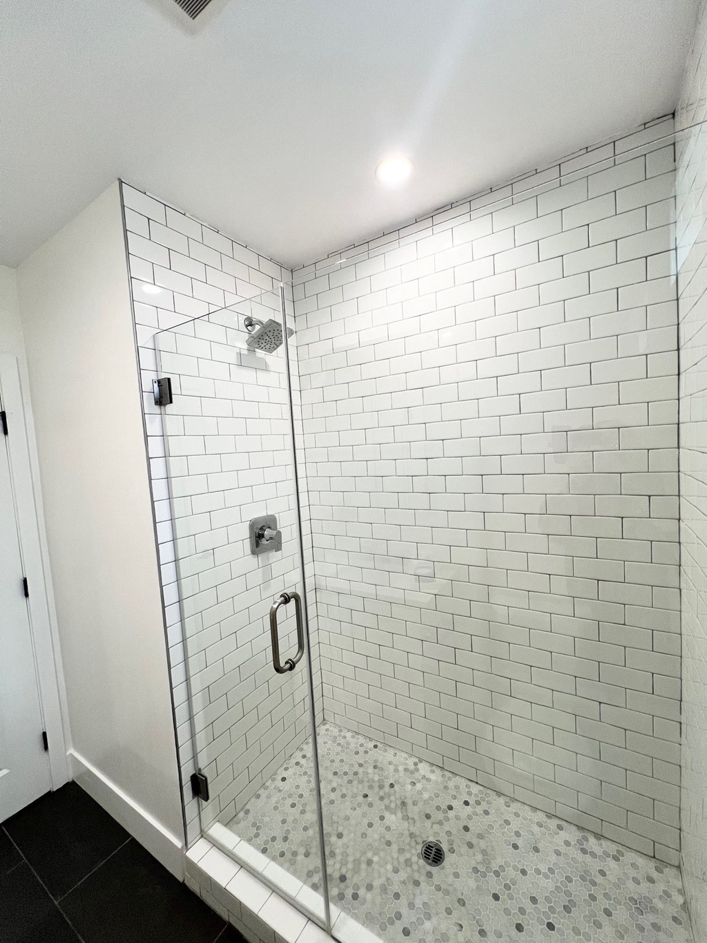 a walk in shower in a white tiled bathroom