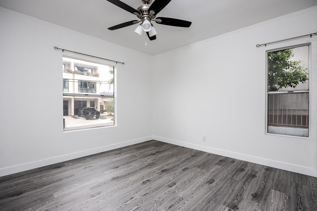 an empty bedroom with a ceiling fan and two windows