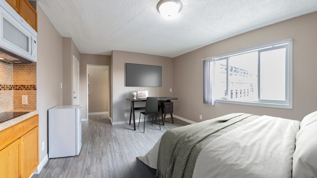 A bedroom with a bed, a table, and a refrigerator.
