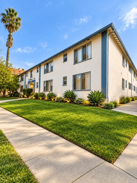 A building with a blue stripe on the side is surrounded by green grass and plants.