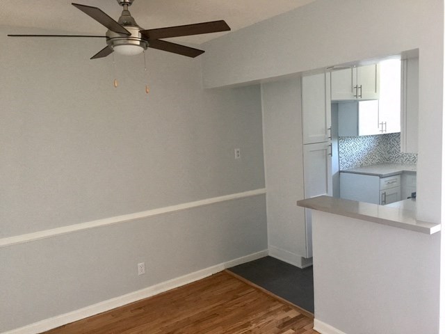 an empty living room with a ceiling fan and a kitchen