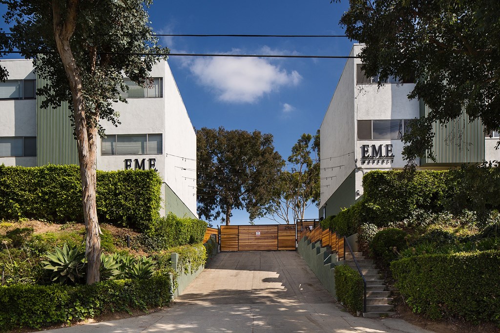 a path between two buildings with trees and a fence