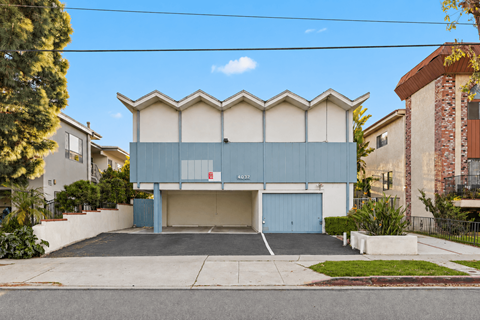 A blue building with a garage door is in front of a tree and a brick building.