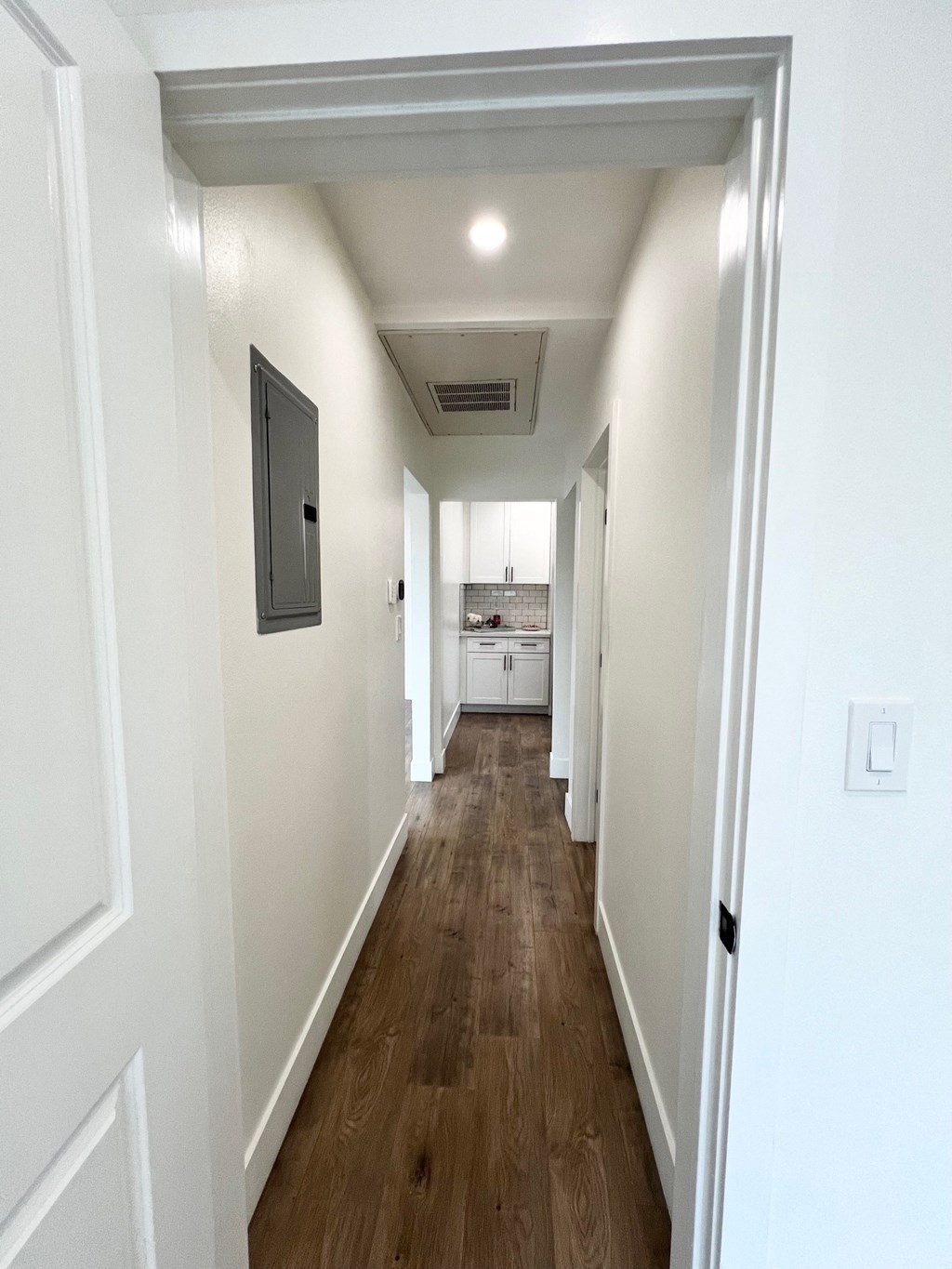 a long hallway with white walls and wood floors and a kitchen in the distance