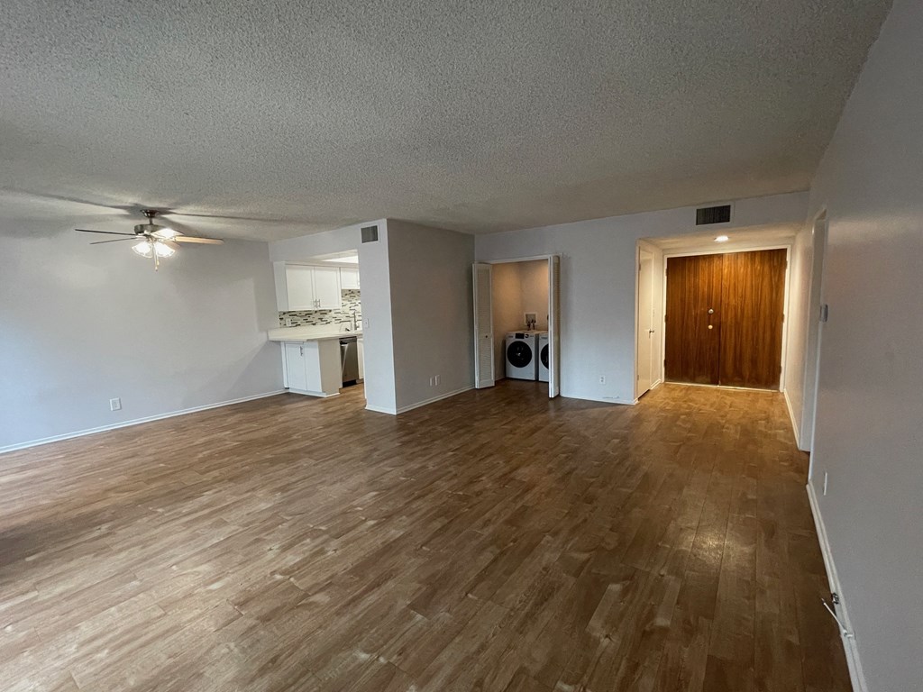 an empty living room with wood flooring and a kitchen