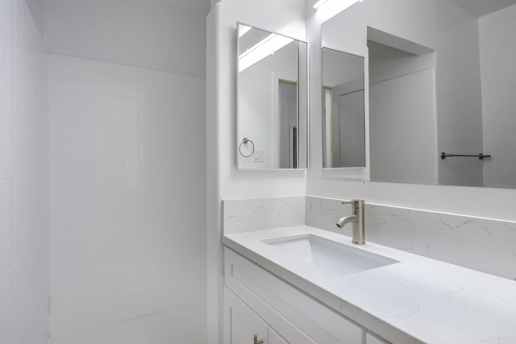 a white bathroom with a sink and two mirrors