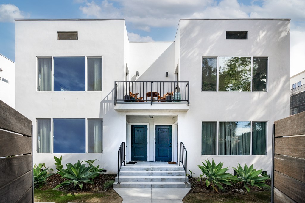 the front facade of a white house with blue doors and a balcony