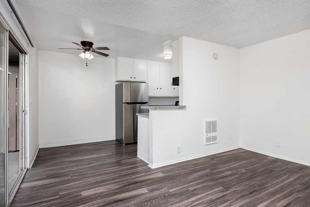an empty living room with a kitchen and a ceiling fan