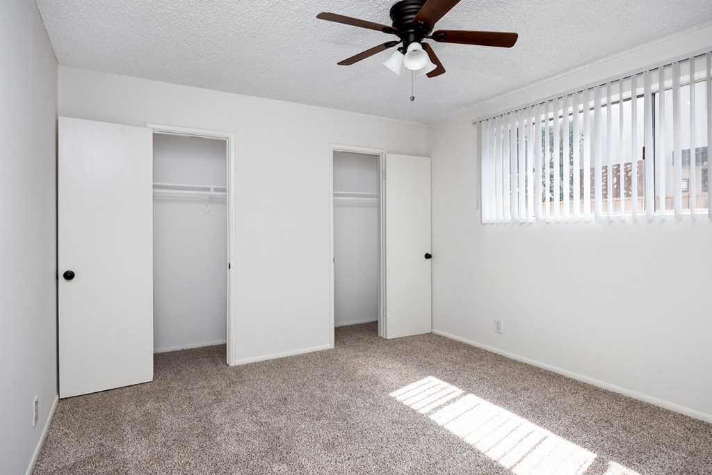 an empty living room with a ceiling fan and two closets