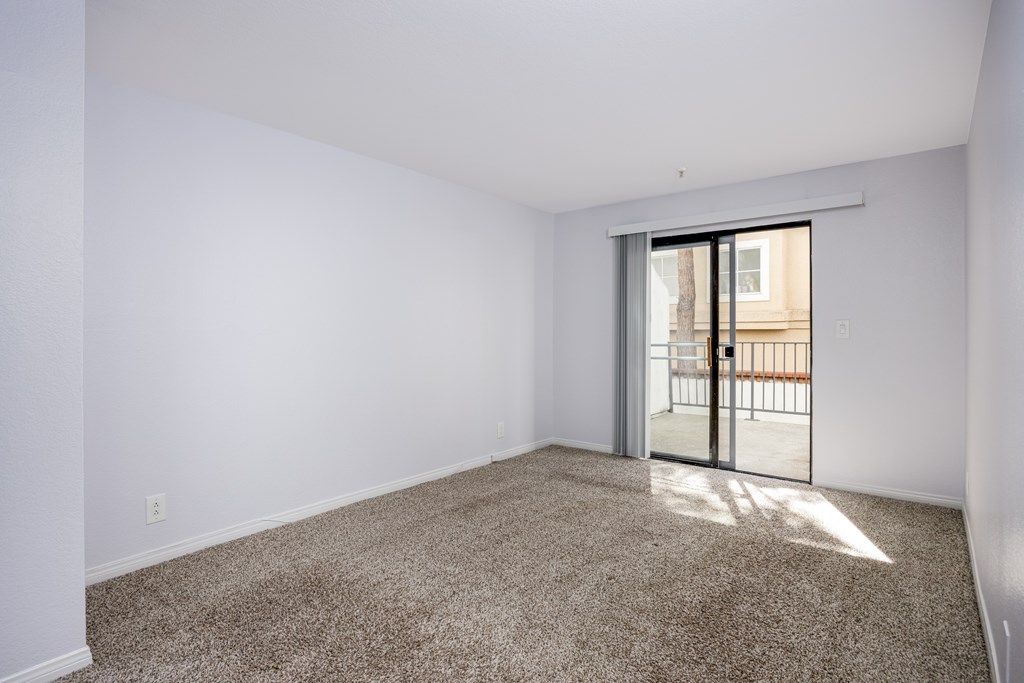 A room with a carpeted floor and a sliding glass door leading to a balcony.