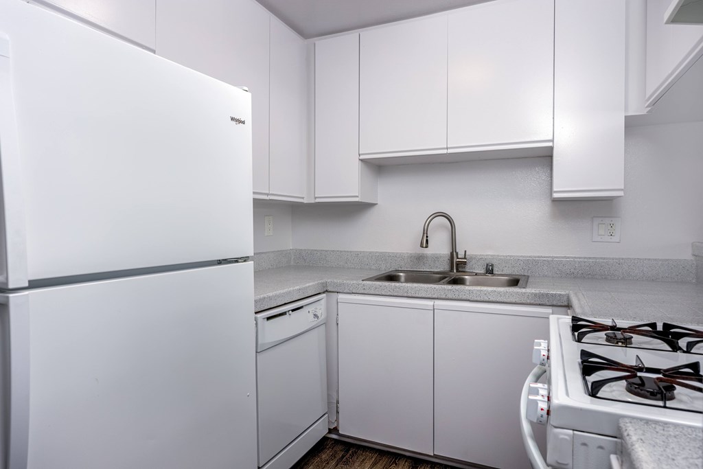 A white kitchen with a refrigerator, sink, and stove.