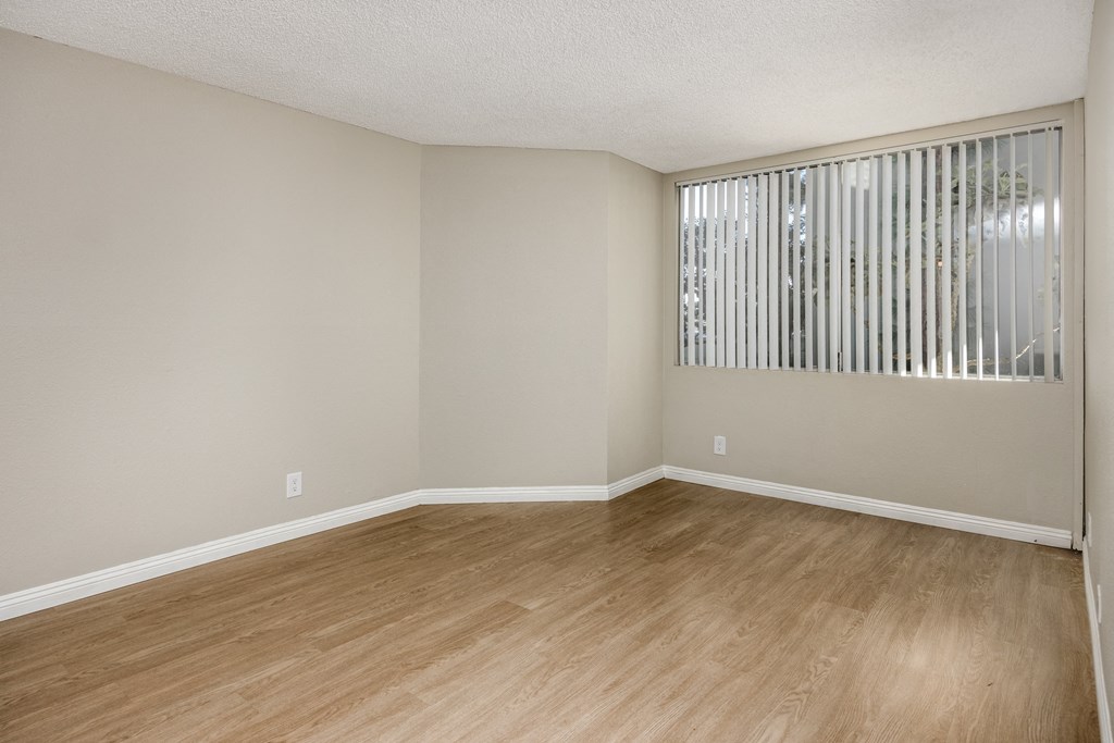 Empty room with wooden floor and a window with blinds.