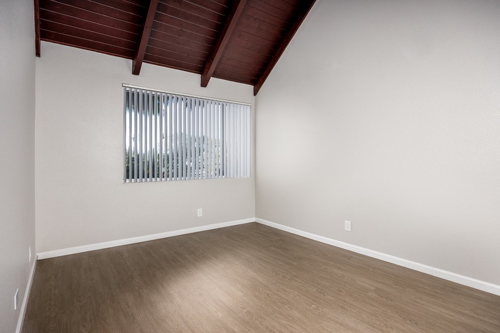 Empty room with wooden floor and a window with blinds.