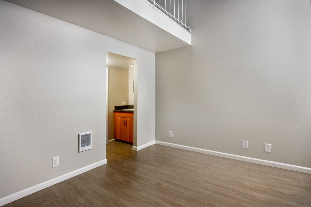 A room with a wooden floor and a white wall with a doorway leading to another room.