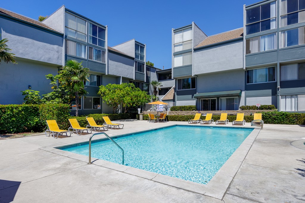 a swimming pool with yellow chairs in front of an apartment building