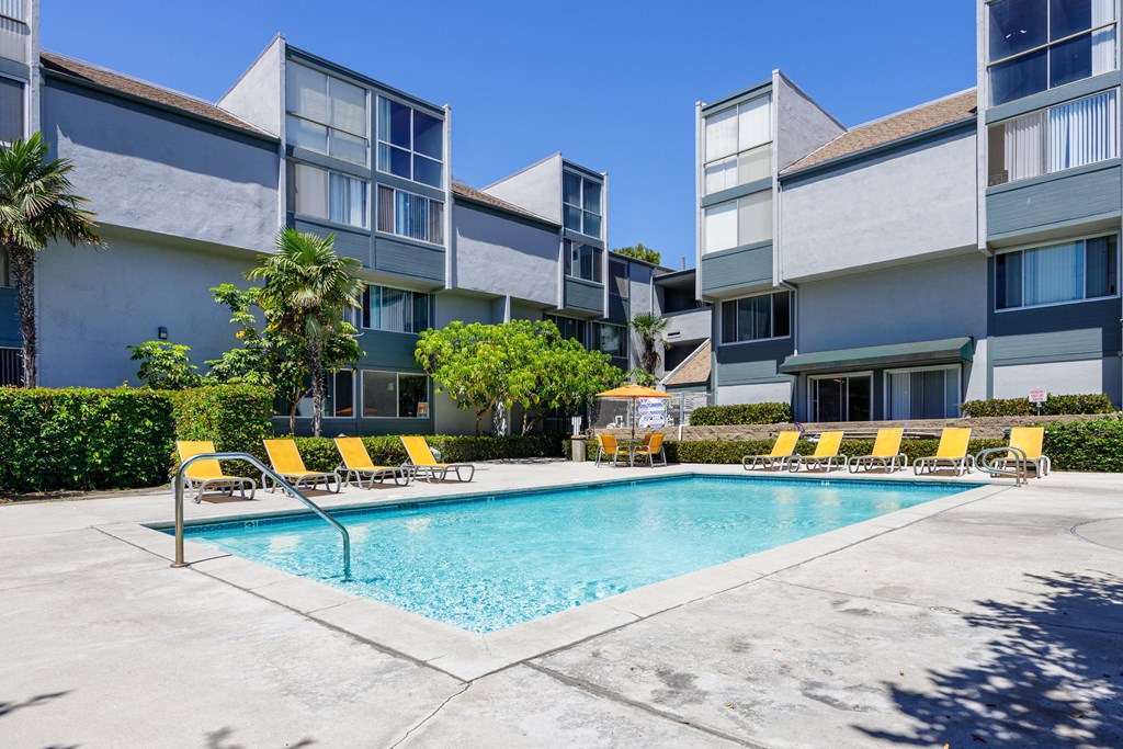 a swimming pool with yellow chairs in front of an apartment building