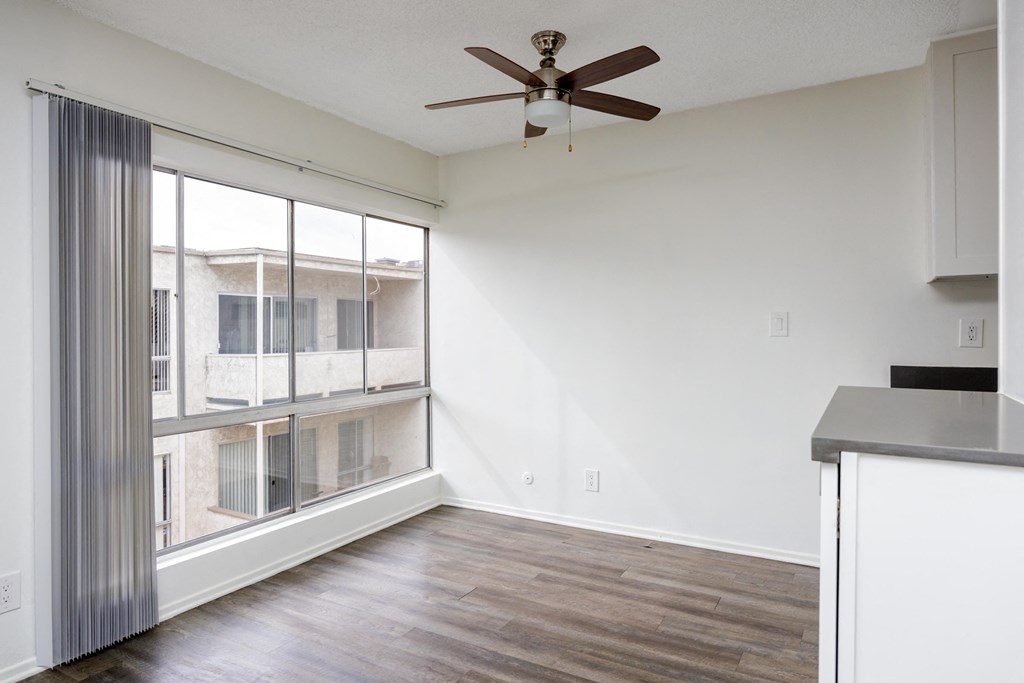 an empty living room with a large window and a ceiling fan