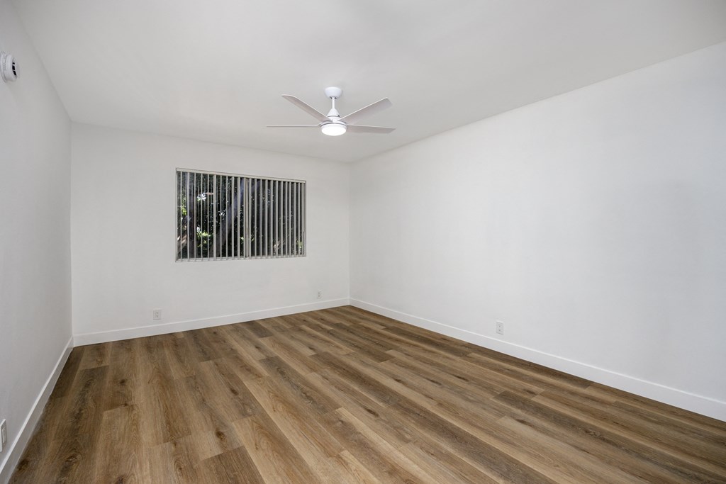 a living room with white walls and wooden floors and a ceiling fan