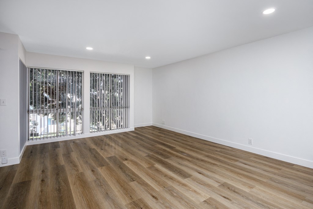 a living room with white walls and wood flooring and a window