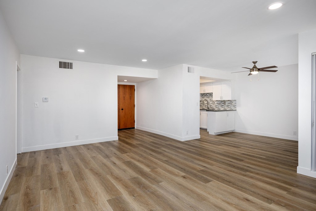 a living room and kitchen with white walls and wood floors