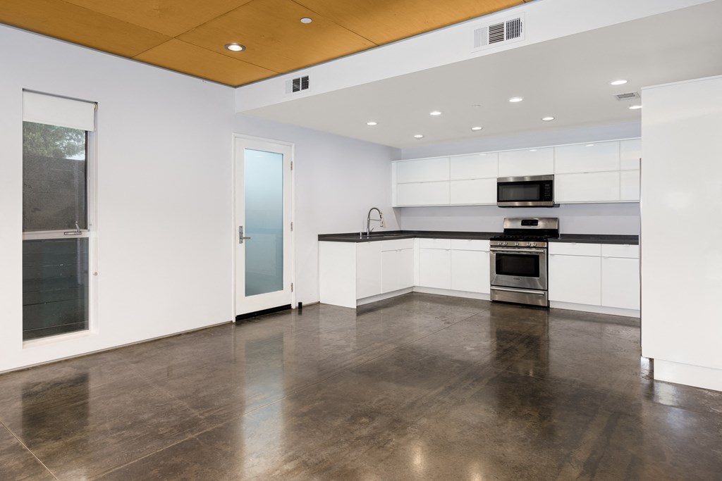 an empty kitchen with white cabinets and stainless steel appliances and a window