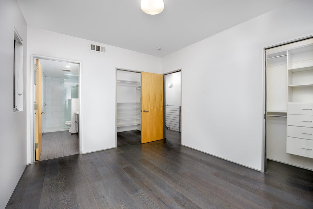 a bedroom with white walls and wood flooring and a door to a closet