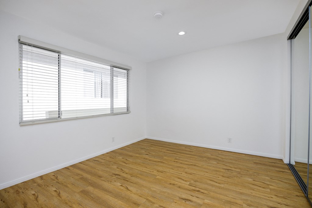 the living room of a home with white walls and wood floors and a window