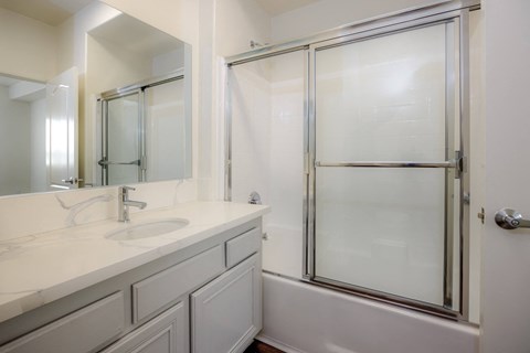 A white bathroom with a sink, mirror, and shower.