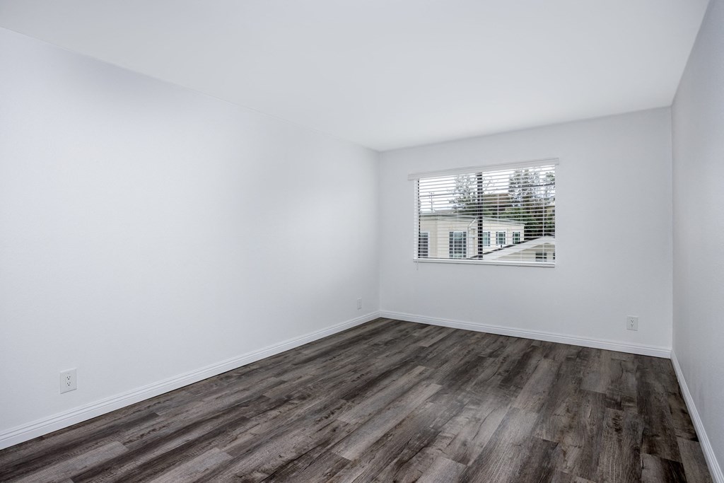 A room with wooden flooring and a window showing a building outside.