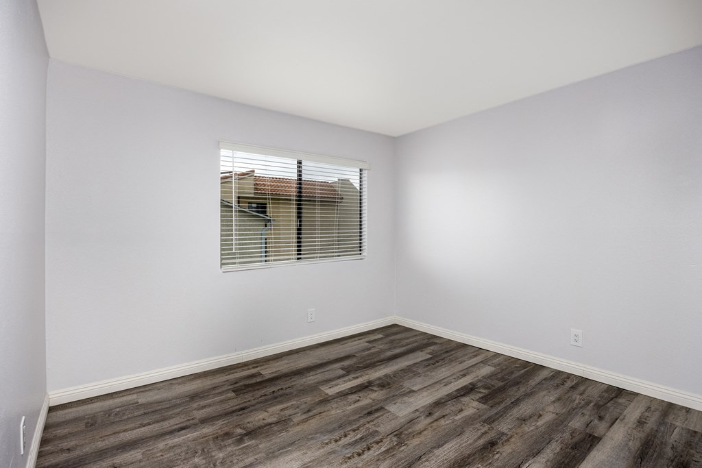 A room with wooden flooring and a window with blinds.