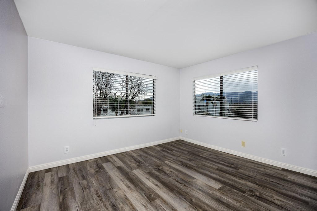A room with wooden floors and two windows with blinds.