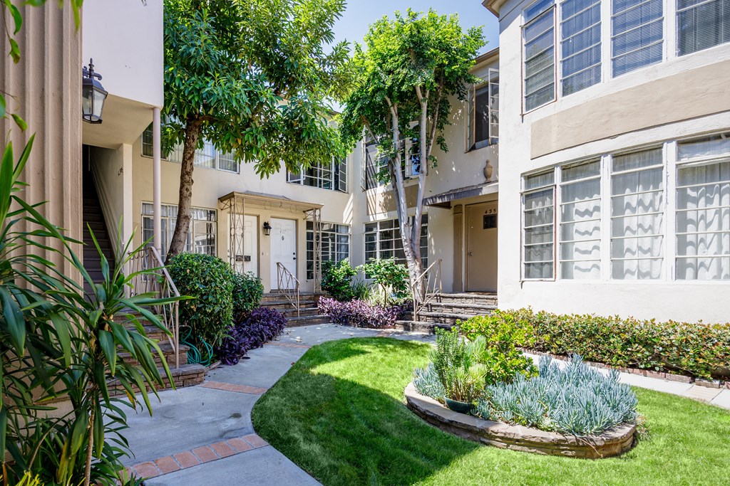 the front yard of an apartment building with green grass and trees