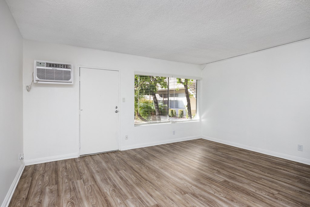an empty room with white walls and wood flooring and a window
