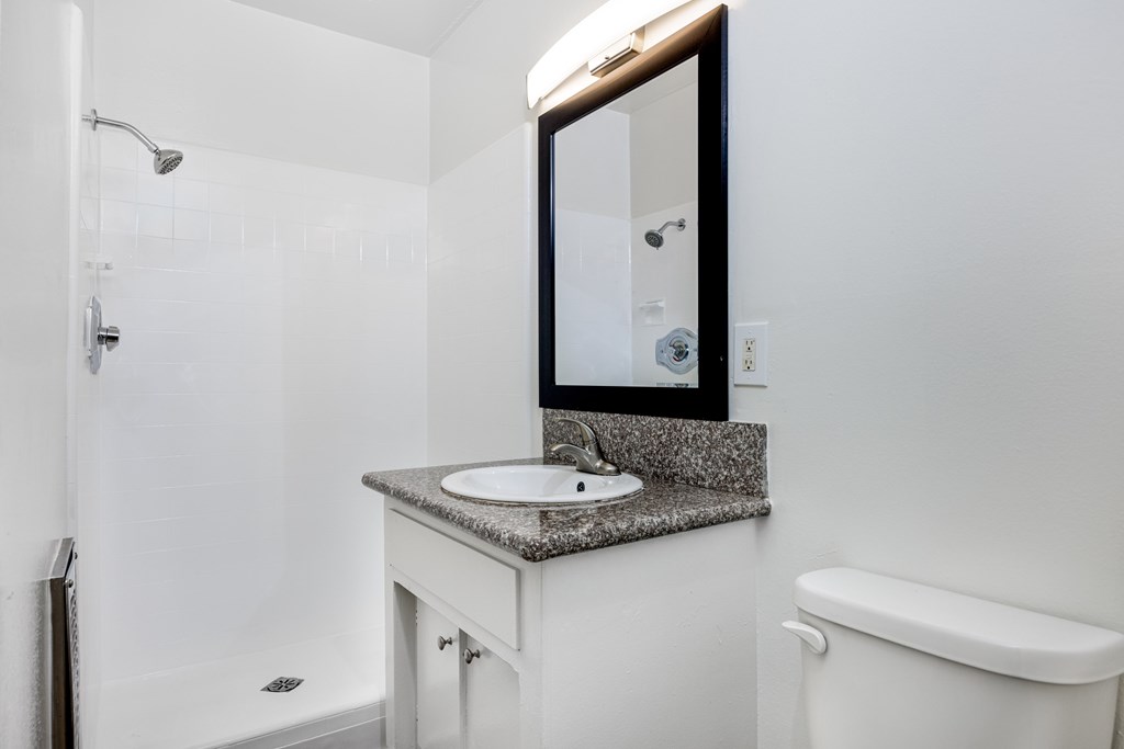 A white bathroom with a sink, mirror, and toilet.