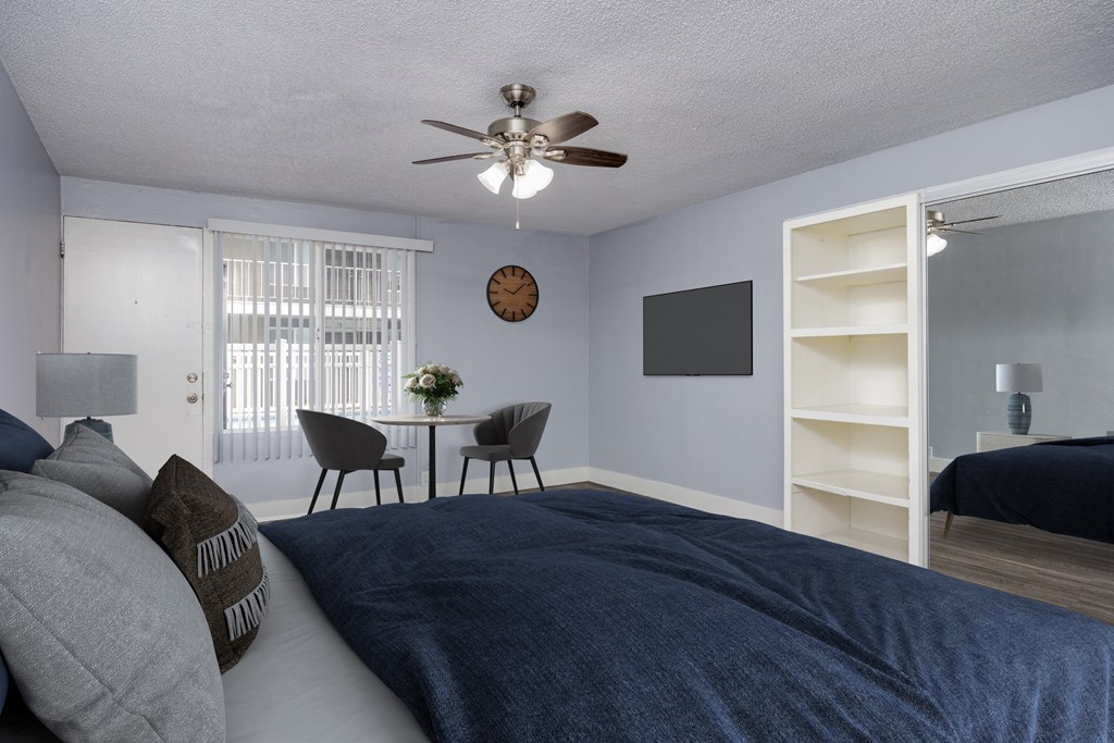 A bedroom with a bed, a chair, a table, and a ceiling fan.