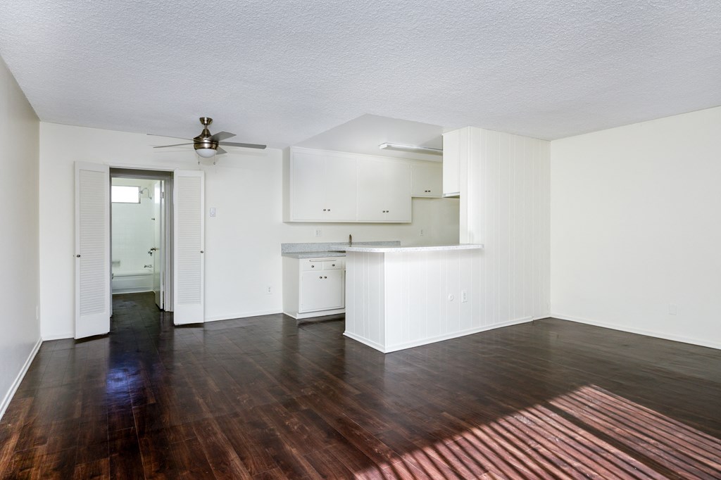 an empty living room and kitchen with hardwood floors and a ceiling fan