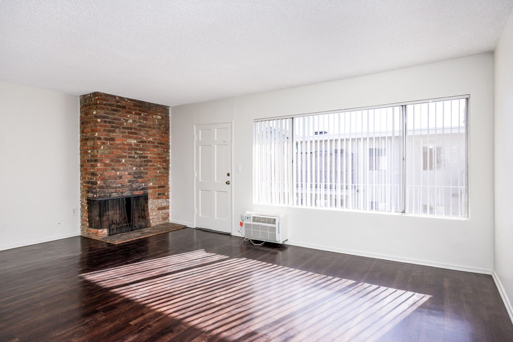 an empty living room with a brick fireplace and hard wood floors