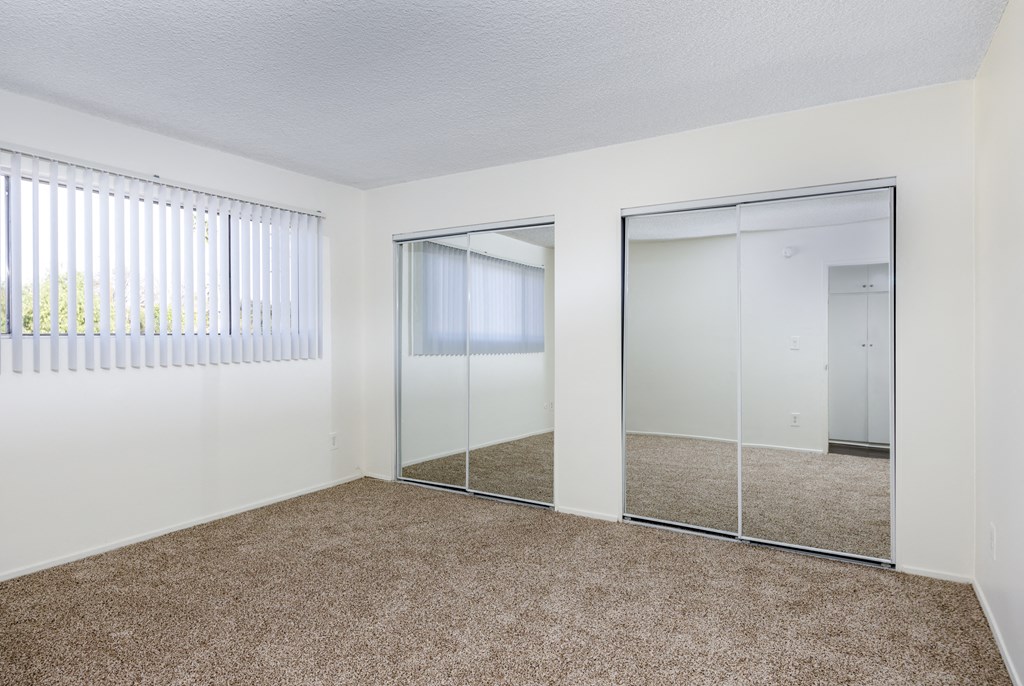 an empty bedroom with mirrored closet doors and carpeting