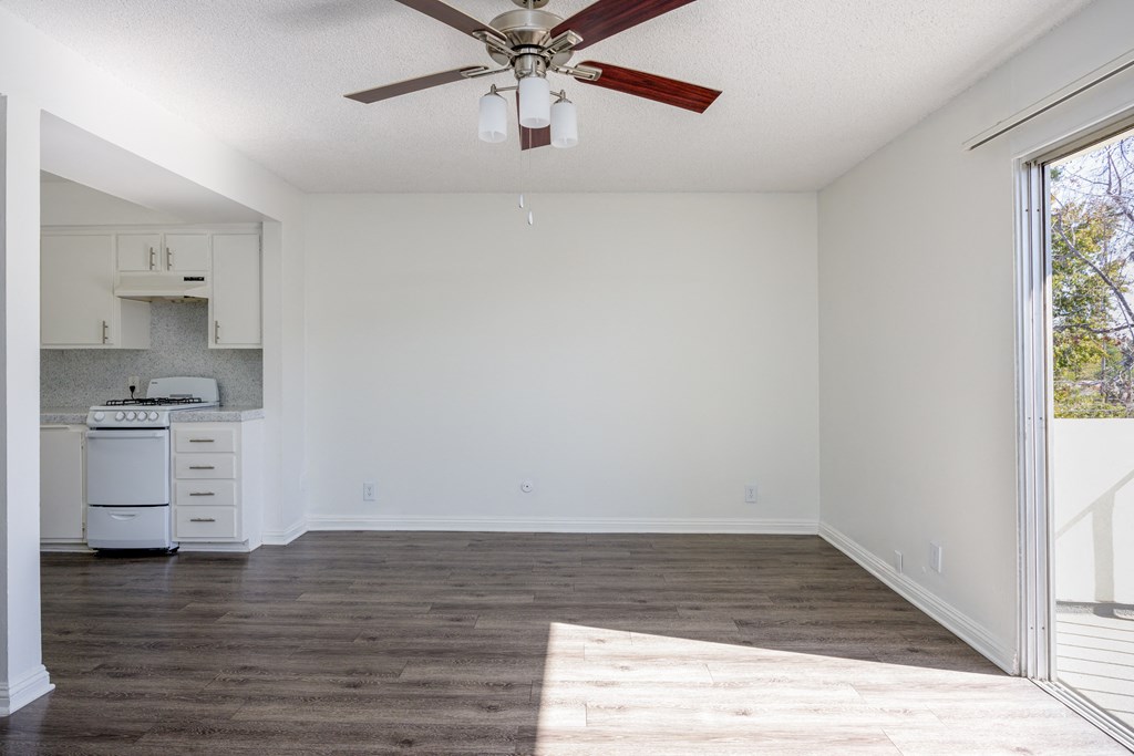 an empty living room with a ceiling fan and a kitchen