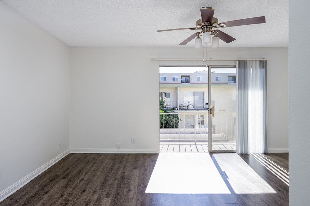 an empty living room with a ceiling fan and a balcony