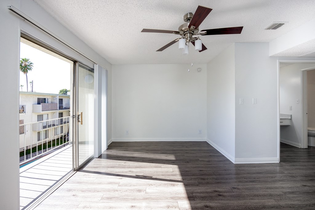 an empty living room with a ceiling fan and a balcony