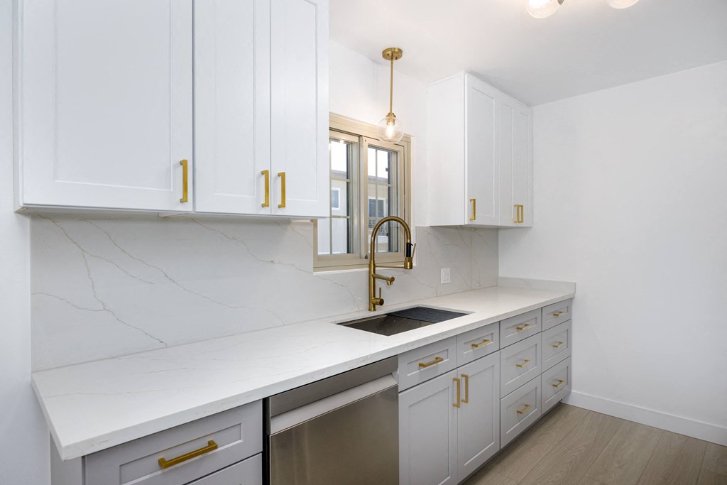 a kitchen with white cabinets and a sink and a gold faucet