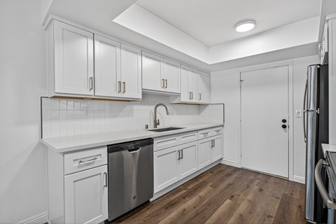 A kitchen with white cabinets and a wooden floor.