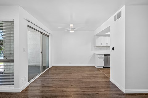 A spacious room with a ceiling fan and a sliding glass door leading to a balcony.